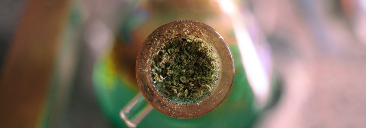 A detailed image of ground cannabis packed in a glass water pipe, highlighting its intricate texture.