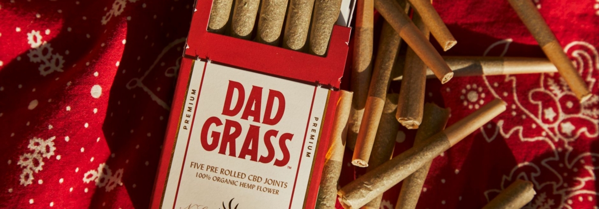 A pack of Dad Grass CBD joints on a red fabric with scattered joints around.
