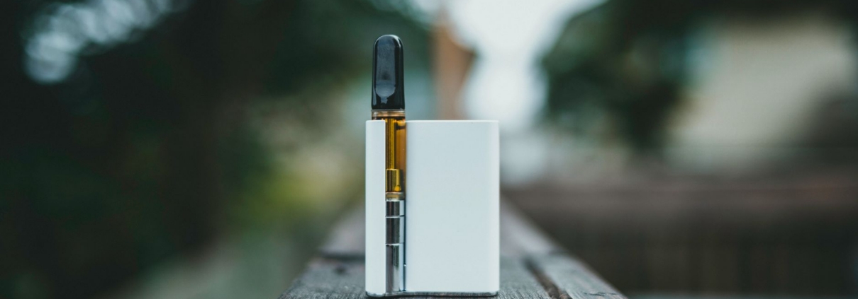 A sleek vape device resting on a wooden surface outdoors in natural light.