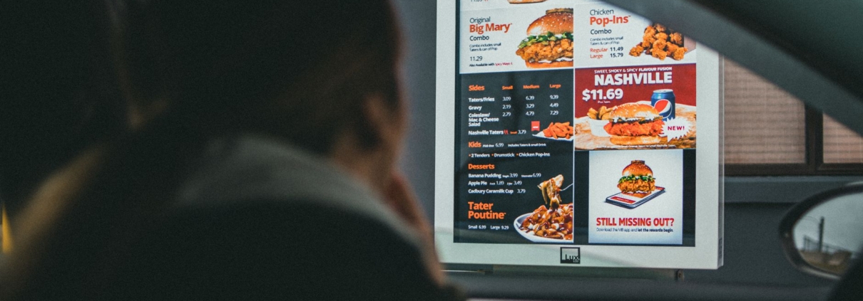 A woman in a car views the menu at a fast food drive-thru, ready to order her meal.