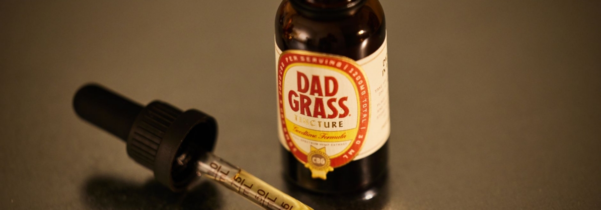An open CBD tincture bottle with a dropper on a reflective surface.