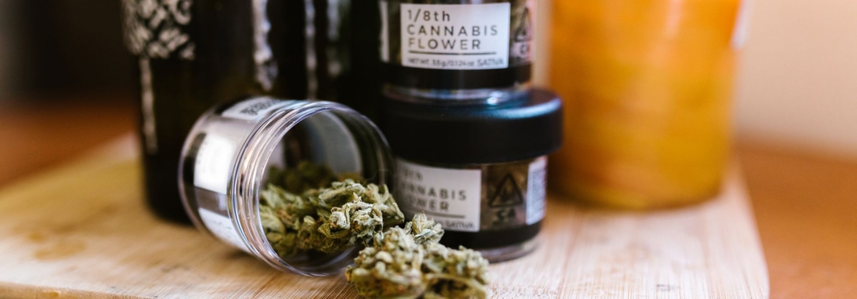 Cannabis buds in glass jars on a wooden board indoors with soft lighting.