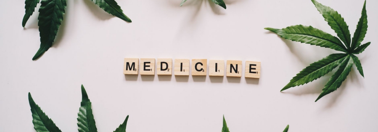 Cannabis leaves arranged with wooden letter tiles spelling 'medicine' on a white surface.