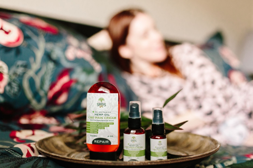 CBD hemp oil pain relief products displayed indoors with a relaxed person in the background.