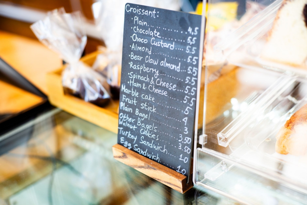 Chalkboard menu listing bakery items like croissants and sandwiches in a cafe setting.
