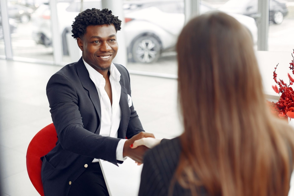 Cheerful happy African American customer in formal elegant suit shaking hands with female dealer after signing papers whil…