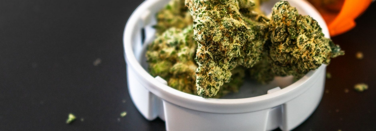 Close-up of cannabis buds spilling from a prescription container, isolated on black background.