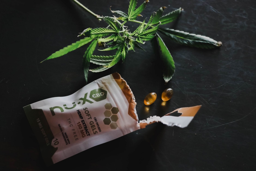 Close-up of CBD softgels with hemp leaves on a dark background.