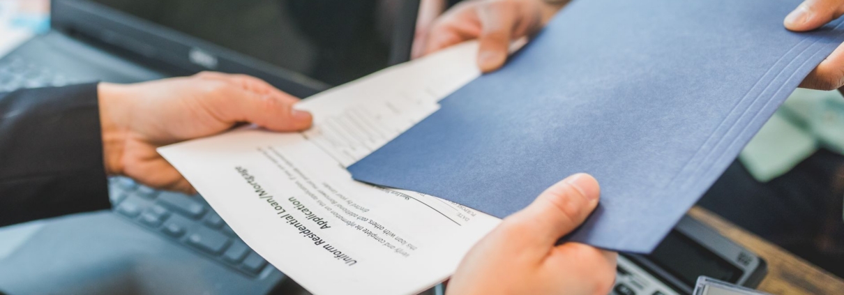 Close-up of hands exchanging real estate documents in an office setting.