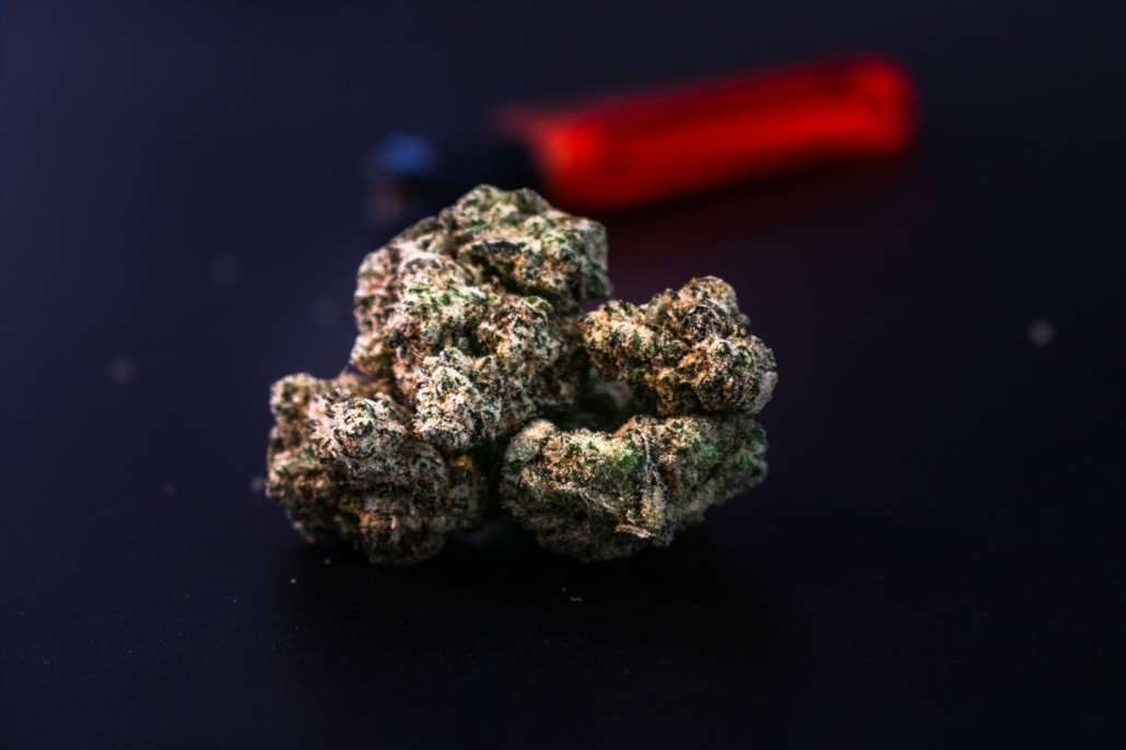 Detailed close-up of a cannabis bud with a red lighter in the background on a dark surface.