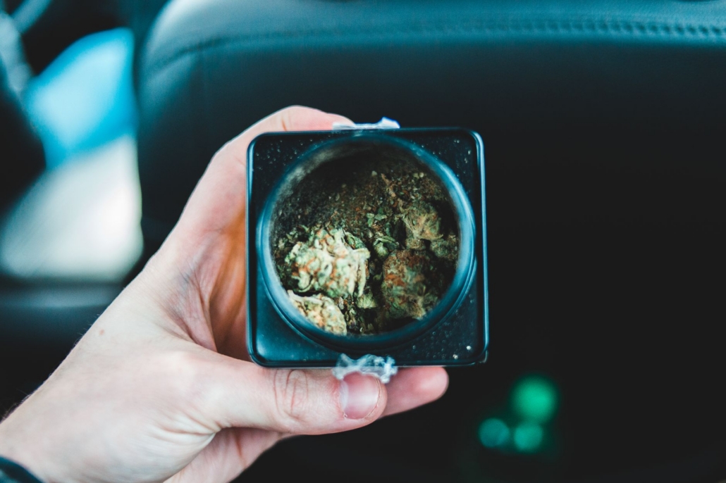 From above anonymous person showing box with marijuana while sitting on back seat of car
