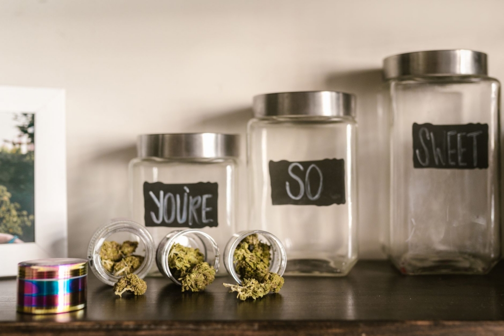 Glass jars filled with cannabis buds artistically arranged on a shelf with playful labels.