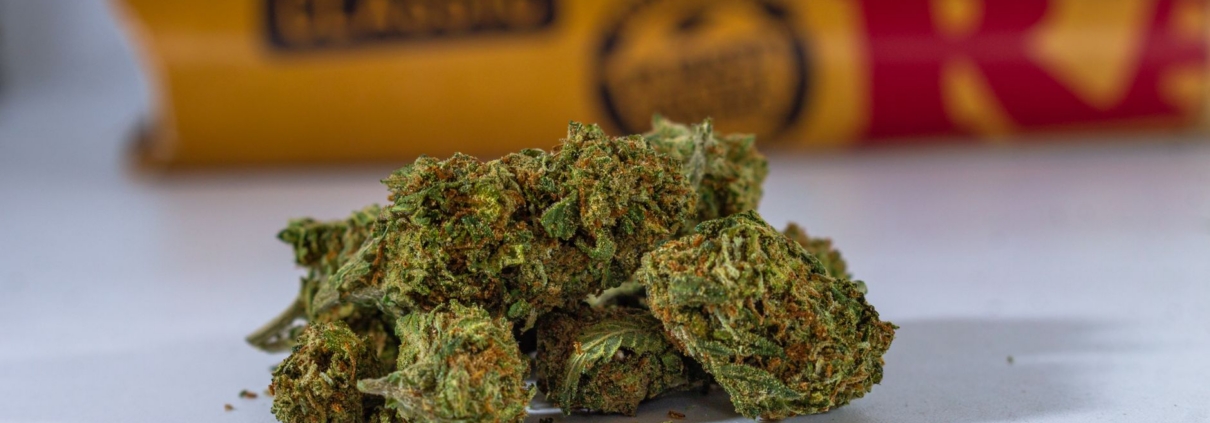 High-quality close-up of cannabis buds with rolling papers in the background on a white surface.