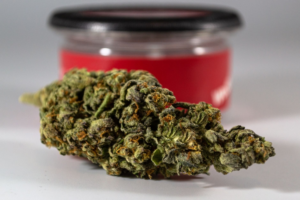 Macro photo of a cannabis bud with a blurred red container in the background.