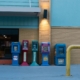 Row of colorful newspaper stands against a brick wall in urban setting during daytime.