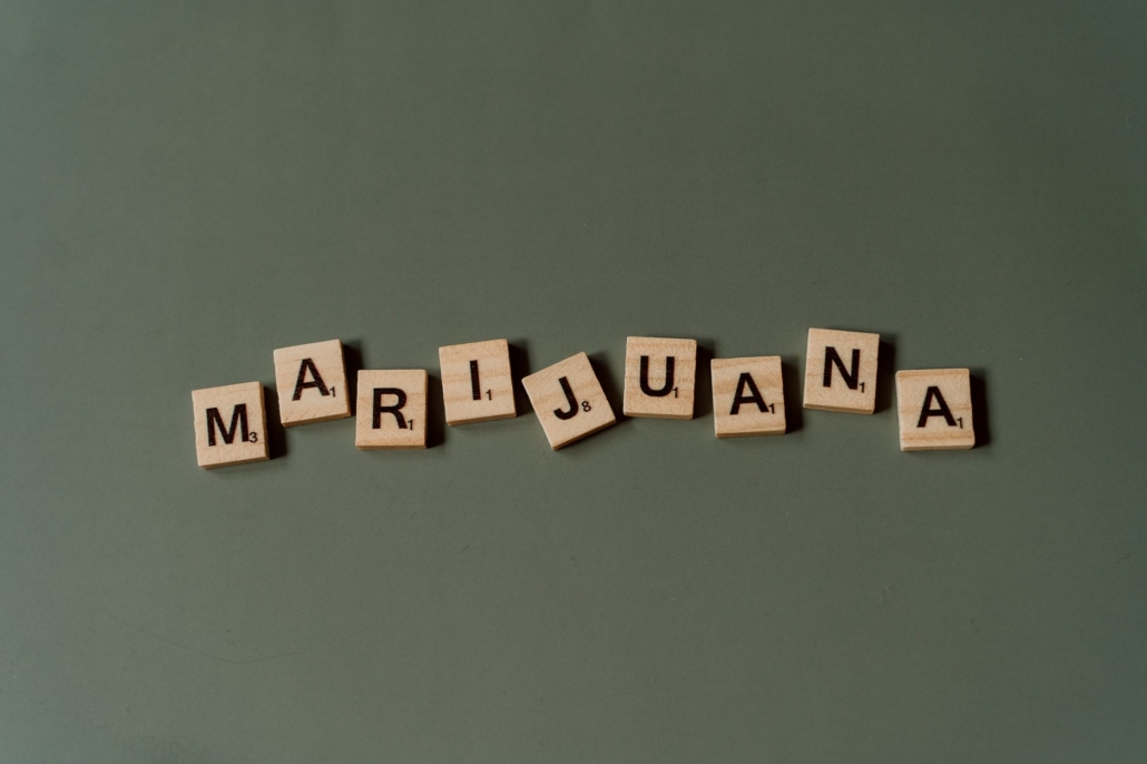 Scrabble tiles arranged to spell 'Marijuana' against a green backdrop in a minimalist style.