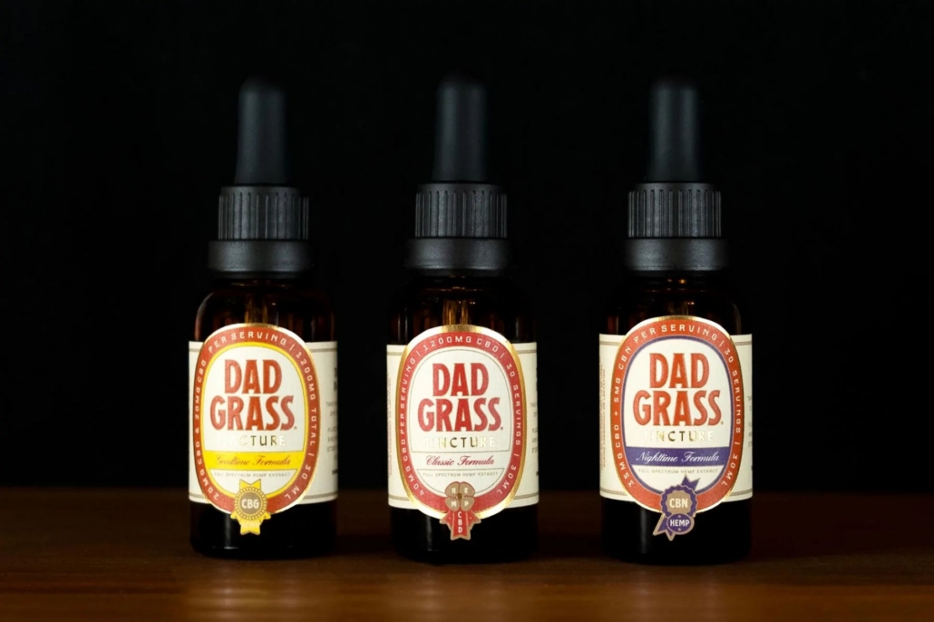 Three bottles of Dad Grass tincture showcasing different formulas on a black background.