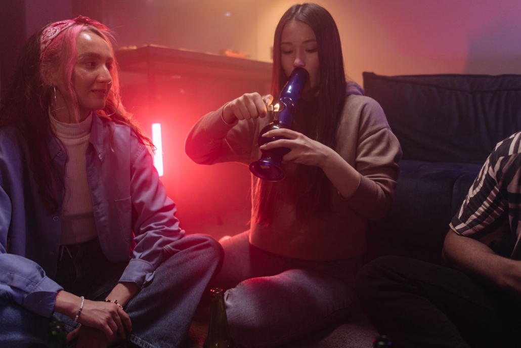 Two women enjoy a relaxed evening indoors with a bong, surrounded by warm lighting.