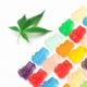 Vibrant gummy bears next to a cannabis leaf on a white background, symbolizing edible cannabis sweets.
