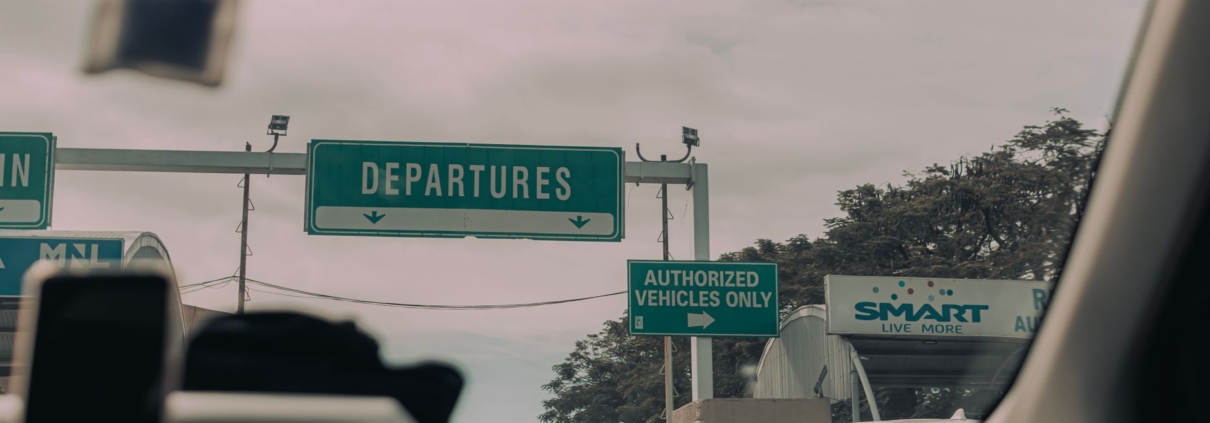 View through windshield of car driving towards airport departure signs and authorized vehicle only lane, captured in soft …