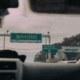 View through windshield of car driving towards airport departure signs and authorized vehicle only lane, captured in soft …